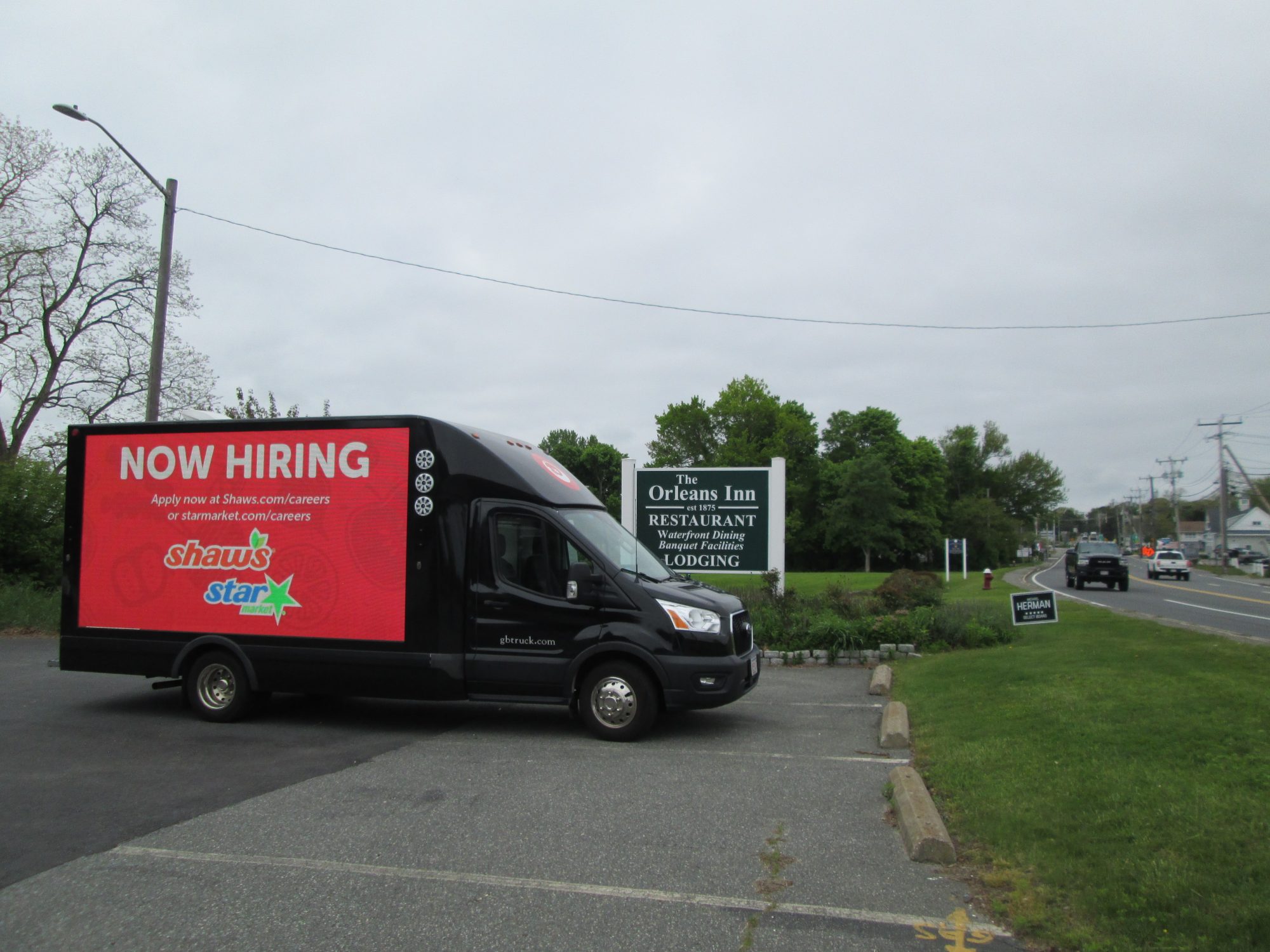 Digital LED mobile billboard truck displaying a NOW HIRING ad, parked along Route 6A in Orleans MA